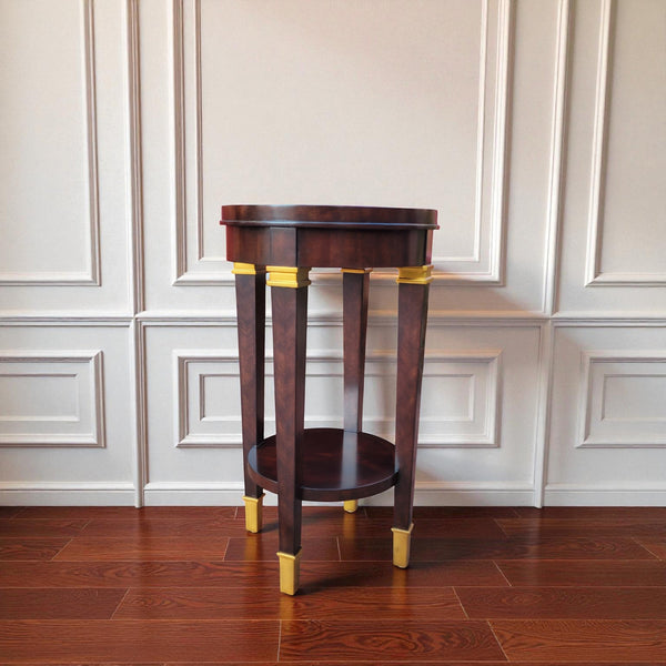 Tradition De France dark wood round accent table with gold accents on tapered legs and lower shelf.